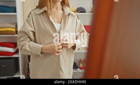 Eine junge Frau schnappt ihren Trenchcoat in einem modernen Kleiderschrank voller bunter Kleidung. Stockfoto