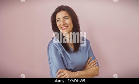 Reife hispanische Frau mit überkreuzten Armen, die vor rosa Hintergrund lächelt Stockfoto