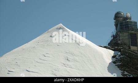 Ein schneebedeckter Berg mit einem Teleskop oben. Der Berg ist sehr steil und der Schnee sehr tief Stockfoto