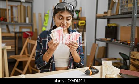 Lächelnde südasiatische Frau, die isländische Währung in einer Holzwerkstatt hält. Stockfoto