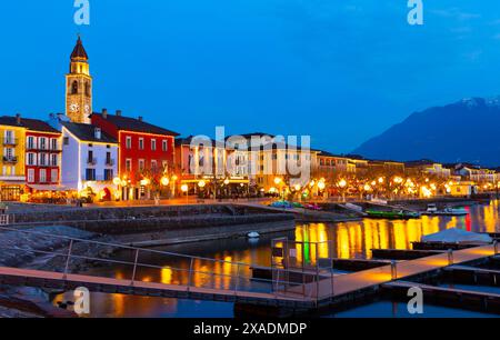 Beleuchtete Promenade in Ascona mit Glockenturm und festfahrenden Booten in der Dämmerung Stockfoto