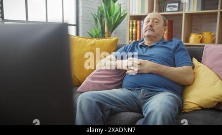 Mann mittleren Alters, der sich im Wohnzimmer auf einer Couch entspannt und zuhause fernsieht. Stockfoto