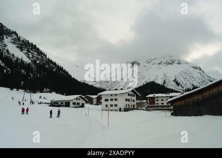 Eine verschneite Bergkette mit einer kleinen Stadt in der Ferne. Die Stadt ist von Schnee umgeben und hat einige Gebäude. Es gibt Leute, die Ski fahren und Snowboarder fahren Stockfoto