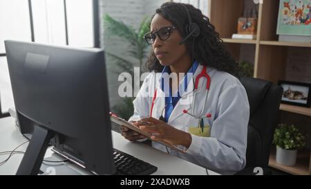Eine junge afroamerikanische Ärztin in einem weißen Mantel mit einem Stethoskop um den Hals wird während der Arbeit an einem Computer in einer Klinik fokussiert. Stockfoto
