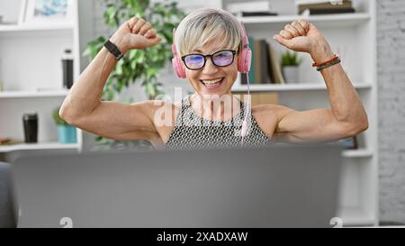 Die energiegeladene Seniorin bewegt die Muskeln mit Kopfhörern in einer modernen Büroumgebung. Stockfoto