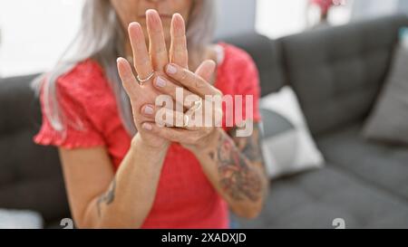 Schöne, reife Frau mit grauem Haar, leidend unter Arthritis und Arthrose Schmerzen, sitzt allein auf ihrem gemütlichen Wohnzimmer Sofa zu Hause, Stockfoto
