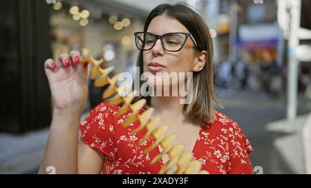 Wunderschöne hispanische Frau, die fröhlich knusprige, leckere Chips auf einem Stock in der takeshita Street, tokio isst - Reisende Junk Food Liebhaber, Sportbrille Stockfoto