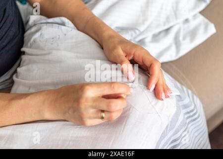 Aufnahme der Frau mit schönen Händen, die einen Leinenstoff aufnäht oder flickt Stockfoto