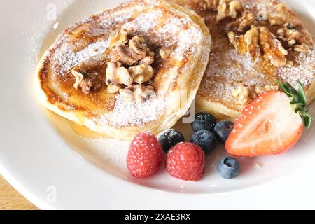 Ein Teller Pfannkuchen mit Walnüssen und Beeren darauf. Der Teller ist weiß und das Essen ist bunt Stockfoto