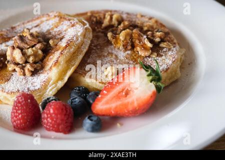 Ein Teller Pfannkuchen mit Heidelbeeren und Erdbeeren darauf. Der Teller ist weiß und das Essen ist bunt Stockfoto
