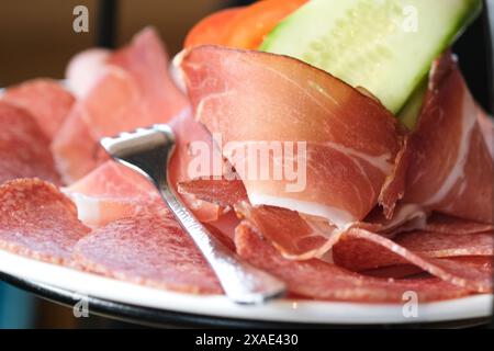 Ein Teller Schinken und Gurkenscheiben mit einer Gabel drauf. Der Schinken wird in kleine Stücke geschnitten und die Gurke in dünne Stücke geschnitten Stockfoto