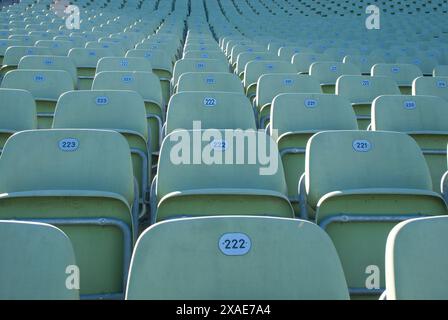 Eine Reihe leerer Sitze in einem Stadion mit Zahlen darauf. Die Sitze sind größtenteils leer, aber es sitzen einige Leute hinten. Das Stadion ist groß Stockfoto