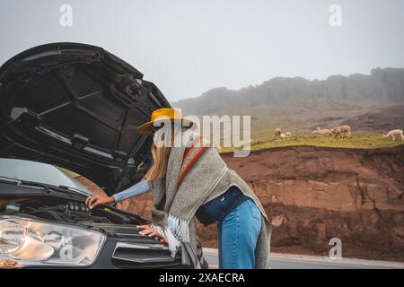 Eine Frau mit gelbem Hut steht neben einem Auto mit angehobener Kapuze, Tourist in Huayllay, Peru. Stockfoto