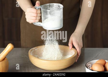 Frau siebt Mehl in eine Schüssel am grauen Tisch, Nahaufnahme Stockfoto