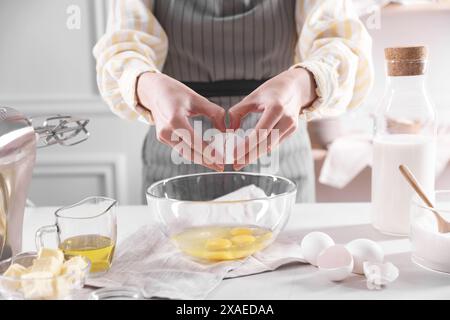 Teig herstellen. Frau bricht Ei am weißen Tisch in der Küche, Nahaufnahme Stockfoto