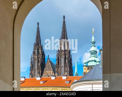 Die Zwillingsspitzen der St. Der Vitusdom erhebt sich majestätisch über der Prager Burg, eingerahmt von einem Bogengang unter einem bewölkten Himmel. Prag, Tschechien Stockfoto