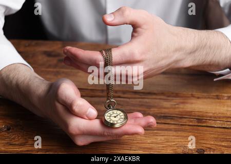 Mann, der eine Kette hält, mit eleganter Taschenuhr am Holztisch, Großaufnahme Stockfoto