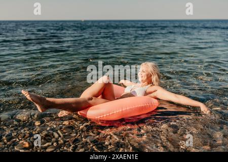 Eine Frau schwimmt auf einem roten Schlauchboot im Ozean. Sie lächelt und genießt den Moment Stockfoto