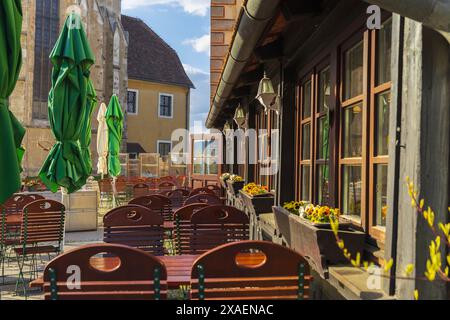 Fotografie einer Terrasse eines traditionellen ländlichen Restaurants mit braunen Stühlen und Tischen und grünen Sonnenschirmen in den österreichischen Alpen Stockfoto