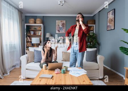 Ein junges Paar ruft die Polizei an, um häusliche Gewalt zu melden. Mann und Frau rufen 911 an, um laute Geräusche von der Wohnung oben zu melden, streiten und schreiende Stimmen. Stockfoto