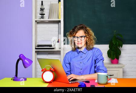 Lehrerjob. Die runzelnde Lehrerin arbeitet mit dem Laptop im Klassenzimmer. Konzentrierter Schüler in Brille, der Webinar auf Laptop ansieht und sich auf vorbereitet Stockfoto