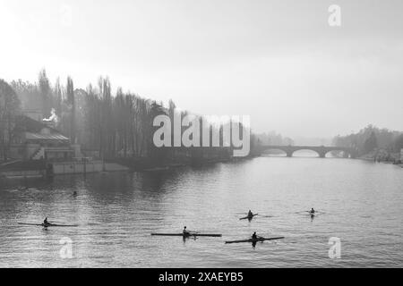 Erhöhter Blick auf eine Gruppe von Ruderern, die auf dem Fluss Po trainieren, mit der Umbert I-Brücke im Hintergrund im Herbst, Turin, Piemont, Italien Stockfoto