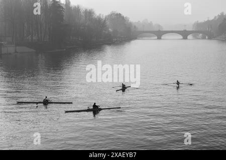 Erhöhter Blick auf eine Gruppe von Ruderern, die auf dem Fluss Po trainieren, mit der Umbert I-Brücke im Hintergrund im Herbst, Turin, Piemont, Italien Stockfoto