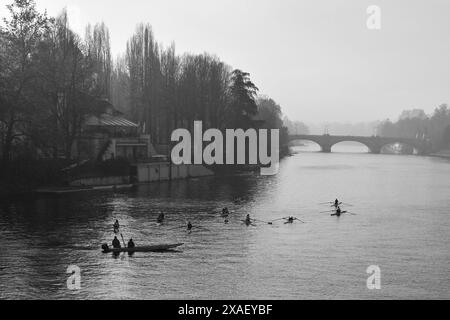 Erhöhter Blick auf eine Gruppe von Ruderern, die auf dem Fluss Po trainieren, mit der Umbert I-Brücke im Hintergrund im Herbst, Turin, Piemont, Italien Stockfoto