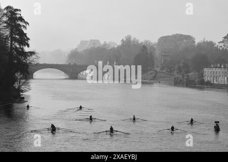 Erhöhter Blick auf eine Gruppe von Ruderern, die auf dem Fluss Po trainieren, mit der Umbert I-Brücke im Hintergrund im Herbst, Turin, Piemont, Italien Stockfoto