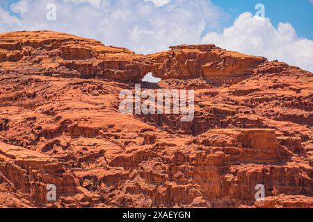 Der atemberaubende natürliche Felsbogen, bekannt als kleine Brücke, steht widerstandsfähig inmitten des atemberaubenden roten Sandes und der zerklüfteten Berge des berühmten Wadi Rum Stockfoto