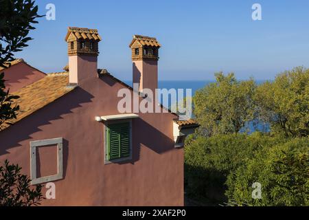 Panoramafoto eines rosafarbenen alten Hauses mit rotem Ziegeldach und Schornsteinen mit Adria am Horizont unter blauem Himmel am sonnigen Sommertag Stockfoto