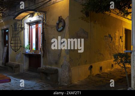 Foto eines alten gelben Gebäudes mit Fischdekor im Zentrum der Küstenstadt Piran in Slowenien bei Nachtlicht Stockfoto