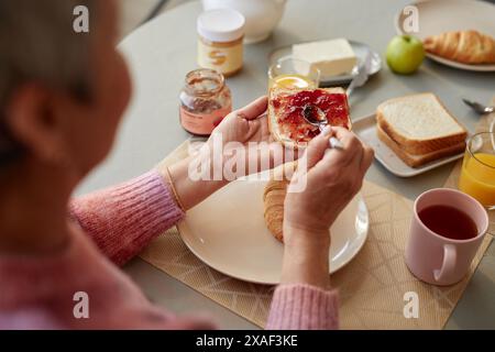 Nahaufnahme einer nicht erkennbaren Seniorin, die Erdnussbutter und Marmelade Sandwich während des Frühstücks im Kopierraum zuhause macht Stockfoto