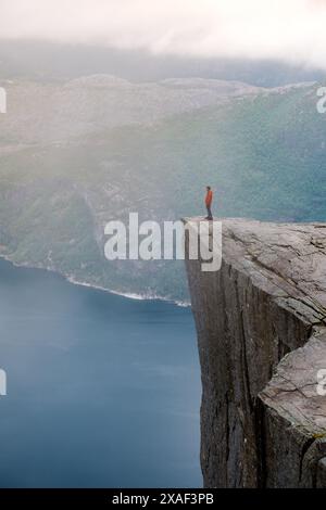 Preikestolen, Norwegen, Eine Einzelperson steht am Rande einer steilen Klippe mit Blick auf einen nebeligen Fjord in Norwegen. Die Weite der Landschaft wird durch die Einzelfigur betont. Preikestolen, Norwegen Stockfoto