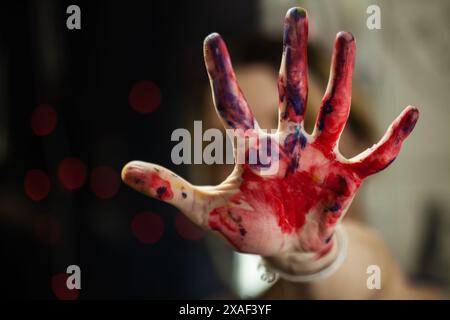 Eine detaillierte fotografische Darstellung von Kreativität und Kunst, die die Hand einer Künstlerin zeigt, die mit leuchtender roter und blauer Farbe gegen eine sanfte Farbe beschmiert ist Stockfoto