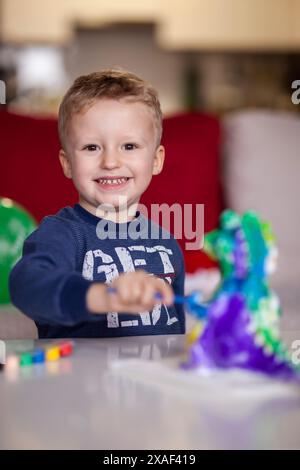 Ein fröhlicher kleiner Junge, der seine Spielzeit mit lebendigen Dinosaurierspielzeugen auf einem Tisch zu Hause genießt und einen glücklichen Kindheitsmoment zeigt. Stockfoto