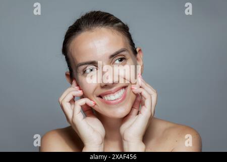 Porträt einer fröhlichen jungen Frau mit strahlenden Augen und einem strahlenden Lächeln, das einen natürlichen und selbstbewussten Look auf grauem Hintergrund zeigt. Stockfoto