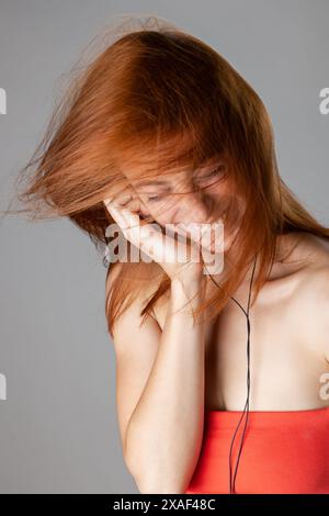 Lebendiges Bild einer glücklichen, jungen Frau mit fließenden roten Haaren, die ihr Gesicht bedeckt und lacht und einen Moment purer Freude und Spontaneität einfängt. Stockfoto