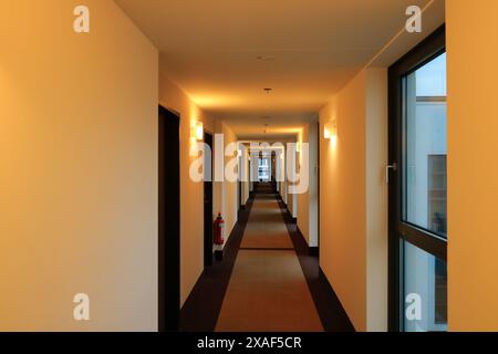 Ein leerer langer Hotelkorridor mit Teppichboden und Lampen beleuchtet die vertikale Innenansicht der Gebäudearchitektur Stockfoto