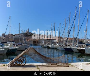 MARSEILLE, FRANKREICH - 19. MAI 2024: Trocknende Fischernetze am Kai des Alten Hafens mit der Basilika Notre-Dame de la Garde im Hintergrund Stockfoto