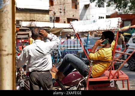 Delhi, Indien: Straßenszene in der Altstadt von Delhi. Rikscha-Fahrer am Telefon wartet auf Kunden Stockfoto
