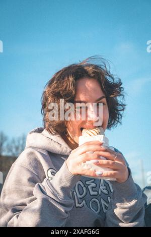 Eine Gruppe von Teenagern sitzt draußen auf einem Basketballfeld mit Ständen, isst Kebab, spielt Basketball, hat Spaß zusammen, hört Musik. Stockfoto