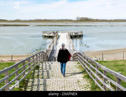 Knokke Heist, Flämische Region - Belgien - 04 03 2021 aktive Frau, die einen hölzernen Pier in einem Naturschutzgebiet entlang der Küste hinunterläuft Stockfoto