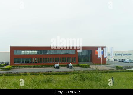 Waregem, Belgien - 22. Mai 2023: Ein modernes Gebäude aus rotem Backstein mit großen Fenstern und Fahnen, von weitem gesehen mit grünem Gras im Vordergrund. Stockfoto