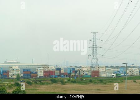 Gent, Belgien - 22. Mai 2023: Ein Blick auf ein belebtes Industriegebiet mit gestapelten Frachtcontainern und einem hoch aufragenden Strompylon gegen einen Überhang Stockfoto