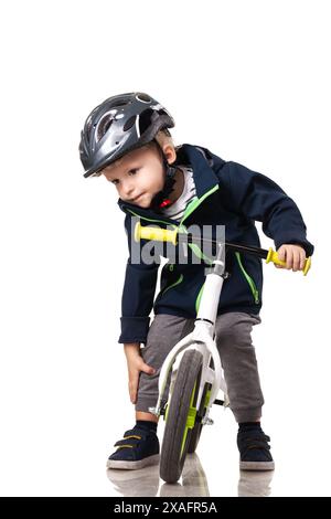 Ein kleiner Junge lernt, ein Balance Bike zu fahren, während er aus Sicherheitsgründen einen Helm trägt. Er scheint konzentriert und entschlossen zu sein. Stockfoto