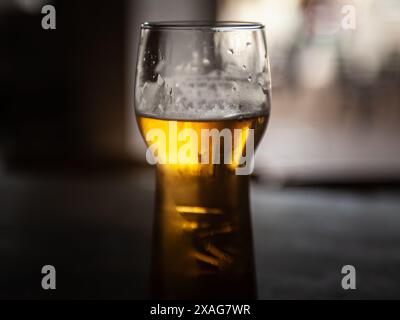 Dieses Bild zeigt eine Nahaufnahme eines gekühlten Glases Bier, das seinen goldenen Farbton und seinen schäumenden Kopf zeigt. Das Bier, ob ein Bier oder ein Bier, verströmt Stockfoto