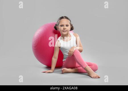 Niedliches kleines Mädchen mit passendem Ball auf grauem Hintergrund Stockfoto