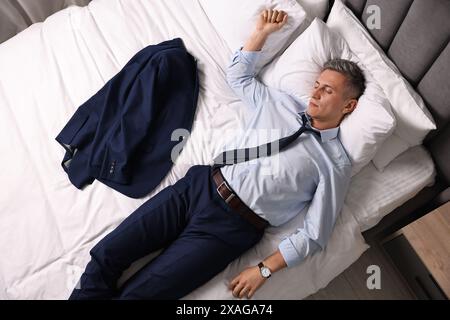 Geschäftsmann in Bürokleidung schläft drinnen auf dem Bett, Blick von oben Stockfoto