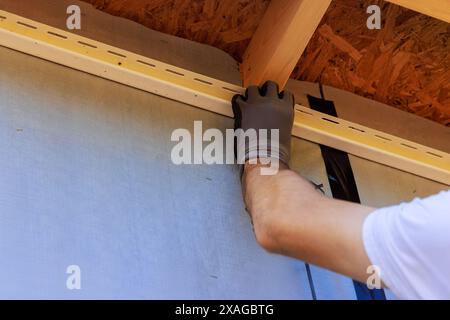 Der Handwerker nagelt J-Kanal Vinylverkleidung vor der Montage für die Verkleidung während des Bauhauses Stockfoto